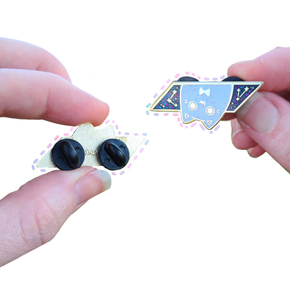 Two hands holding a small cat pins with black and gold details on a white background