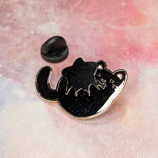 Black cat-shaped enamel pin on a pink and white background